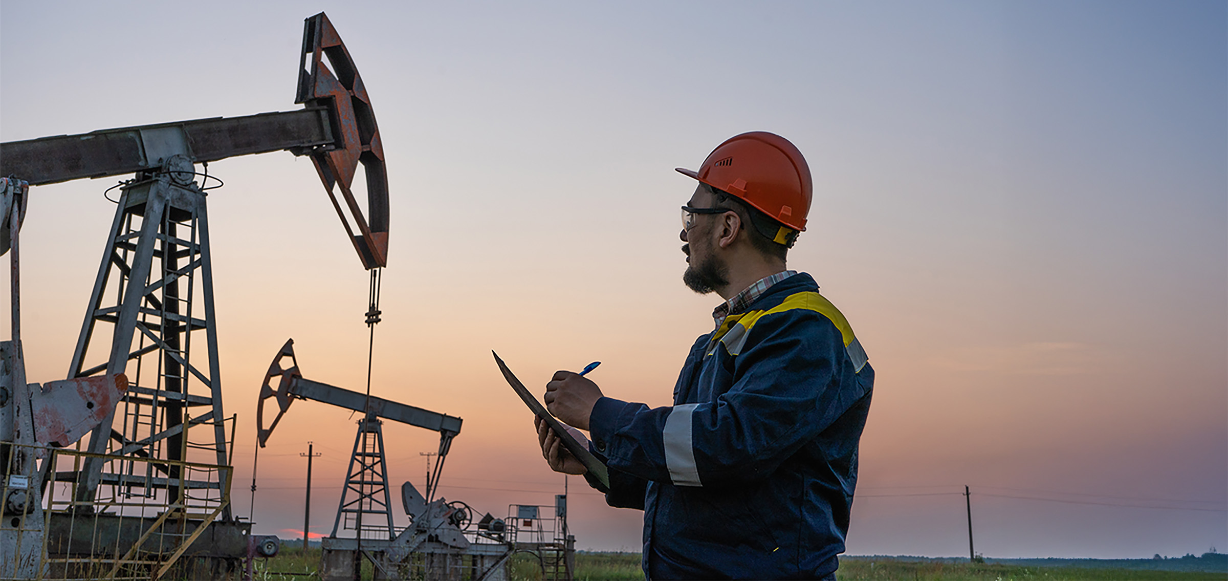 Oil worker checks an oil rig at sunset. Maintenance of oil pump jacks