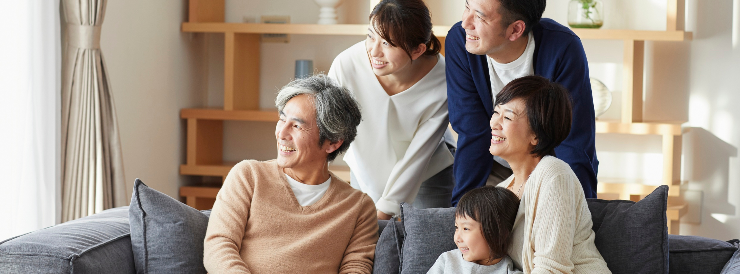 A happy family sitting together in their living room, holding a board above their heads like a roof, symbolizing protection and security provided by BC home insurance from Westland Insurance.