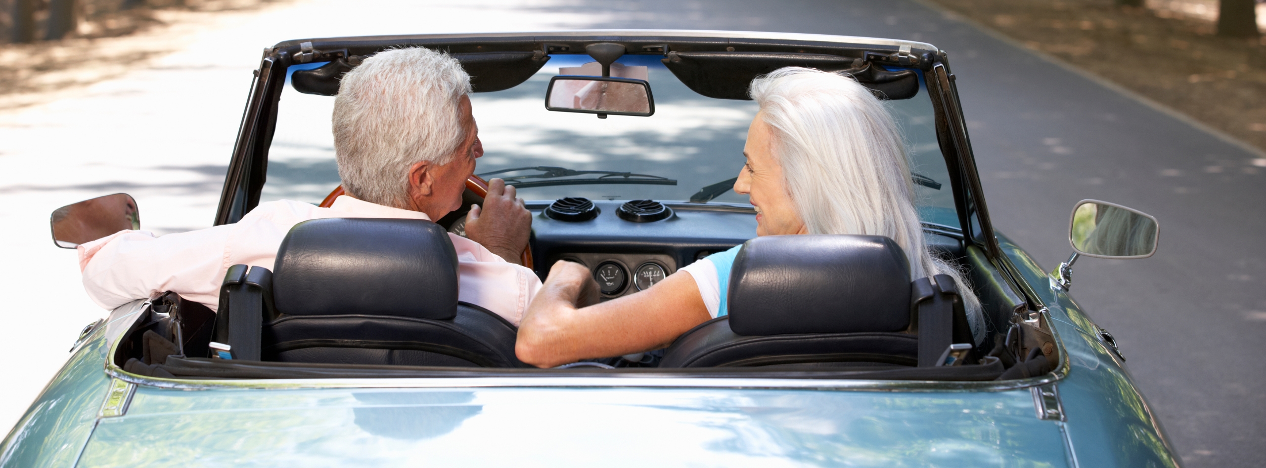 Senior couple driving a classic convertible on a scenic road, representing the added protection available through private car insurance in BC from Westland Insurance.